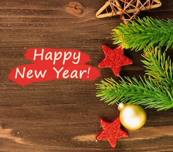 New Year\'s Day decoration, golden ball, fir branches and red stars on wooden background with text Happy New Year on red. Flat lay. Copy space for text. View from above.