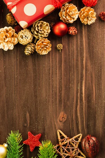 Christmas and New Year\'s Day decoration, balls, fir cones, branches and wooden stars with present wrapped in red paper with golden circles on wood background. Flat lay. View from above. Copy space for text.