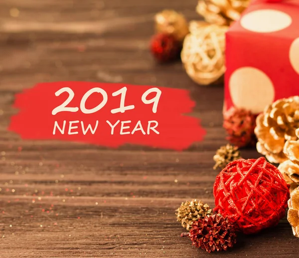 Christmas and New Year\'s Day festive decoration, red and golden balls, fir cones with present wrapped in red paper with golden circles on brown wood background with text 2019 New Year on red