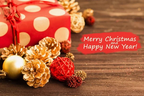 Christmas and New Year\'s Day decoration, balls, fir cones with present wrapped in red paper with golden circles on wood background with text Merry Christmas and Happy New Year on red