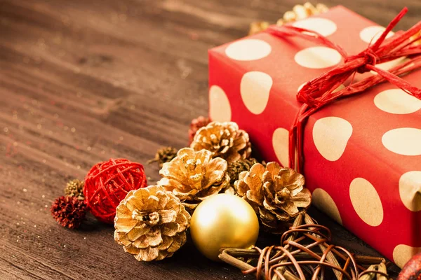 Christmas and New Year\'s Day decoration, golden balls and fir cones, wooden star with present wrapped in red paper with golden circles on brown wood background. Copy space for text.