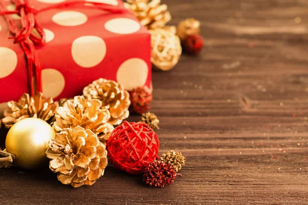 Christmas and New Year\'s Day decoration, golden balls and fir cones, wooden star with present wrapped in red paper with golden circles on brown wood background. Copy space for text.