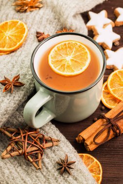 Kış ve yılbaşı tema. Noel çay baharatlar, portakal, tarçın, anason, yıldız, çam kozalakları, biber ve ahşap arka plan üzerinde gri eşarp şeklinde kurabiye ile çay.