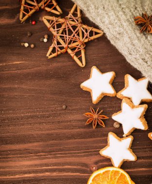Kış ve yılbaşı tema. Baharatlar, portakal, tarçın, anason, yıldız, biber, ahşap yıldız ve ahşap arka plan üzerinde gri eşarp şeklinde kurabiye. Metin için yer kopyalayın. Yukarıdan görüntüleyin. Düz yatıyordu.