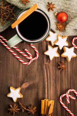 Noel dumanı tüten fincan sıcak ışıltı şarap ile baharat, tarçın, anason, yıldız, kırmızı şeker, biber ve ahşap arka plan üzerinde gri eşarp şeklinde kurabiye. Metin için yer kopyalayın. Yukarıdan görüntüleyin. Düz yatıyordu.