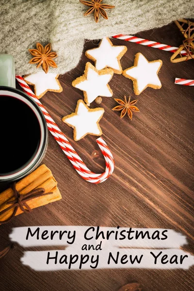 Hot steaming cup of glint wine with spices, anise, cinnamon, cookies in a shape of star, red candies, pepper on wooden background with text Merry Christmas and Happy New Year. Flat lay. View from above.