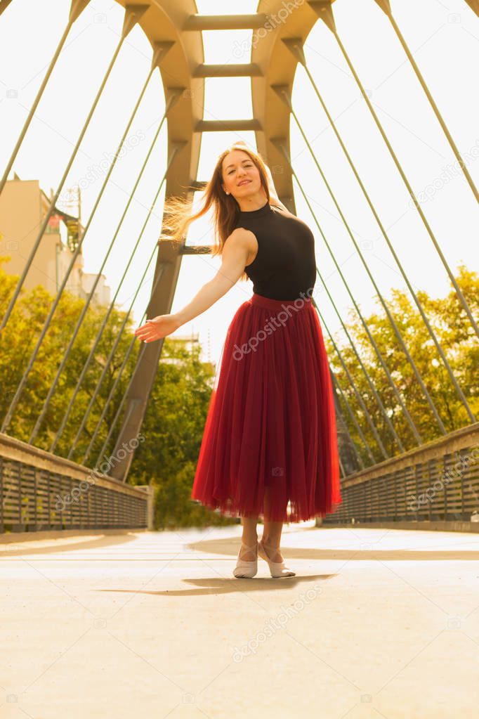 Young slim beautiful woman with long brown hair dancing and smiling outdoors in black shirt and terracotta (red pear) long skirt. Sport and healthy concept.