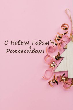 Noel ve yeni yıl gün festival dekorasyon, pembe bir arka plan üzerinde altın şeritler ile ahşap Noel ağacı. Metin için yer kopyalayın. Düz yatıyordu. Gelen yukarıdaki metin ile neşeli Noel ve mutlu yeni yıl (Rusça görüntülemek).