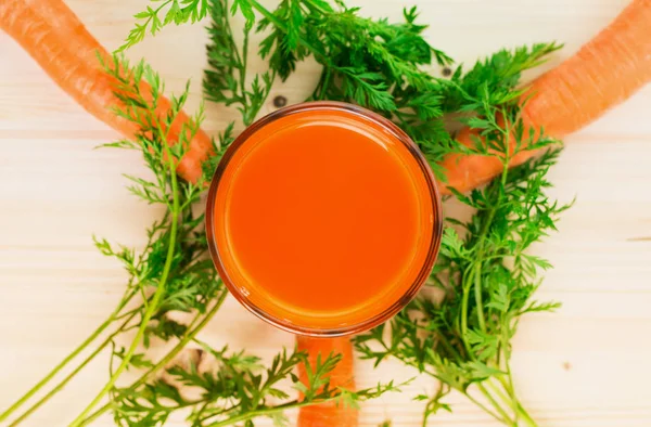 Fresh carrot juice in glass with carrots and green carrot tops on wooden table background. Healthy lifestyle concept. View from above. Flat lay.