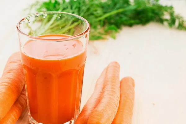 Fresh carrot juice in glass with carrots and green carrot tops on wooden table background. Healthy lifestyle concept. Copy space for text.