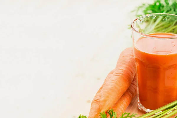 Fresh carrot juice in glass with carrots and green carrot tops on wooden table background. Healthy lifestyle concept. Copy space for text.