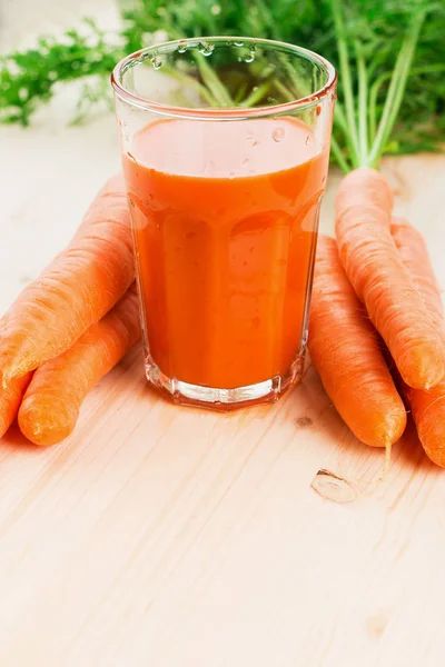Fresh carrot juice in glass with carrots and carrot tops on wooden table background. Healthy lifestyle concept. Copy space for text.