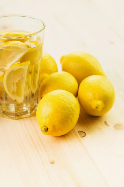 レモンの切れ端や新鮮な手のガラスと水のガラスは 木製の背景にレモンでレモネードを作った コピーのテキストのための領域 — ストック写真