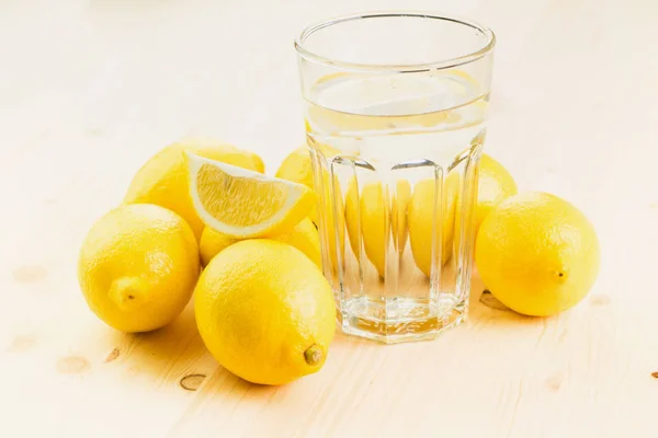 レモンの切れ端や新鮮な手のガラスと水のガラスは 木製の背景にレモンでレモネードを作った コピーのテキストのための領域 — ストック写真