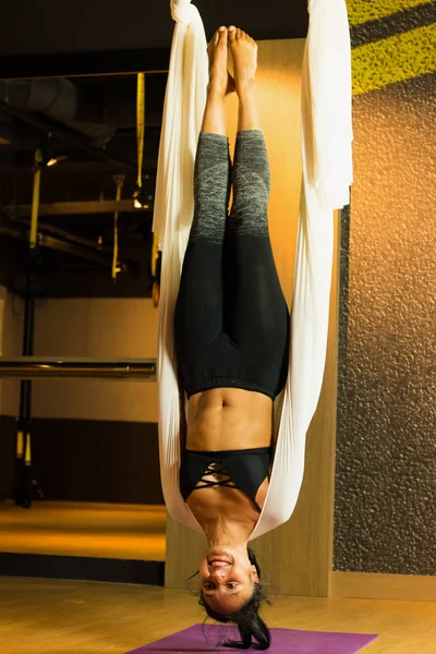 Young woman practicing aerial yoga in fitness studio in white hammock and black clothes - aerial yoga meditating and stretching pose. Healthy and sport concept.