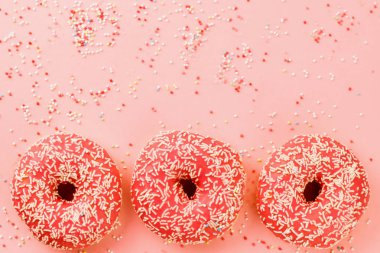 Üç mercan çörek. Çörek pembe bir arka plan üzerine krema ile.