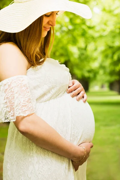 Lycklig gravid kvinna poserar över grön natur bakgrund Stockfoto