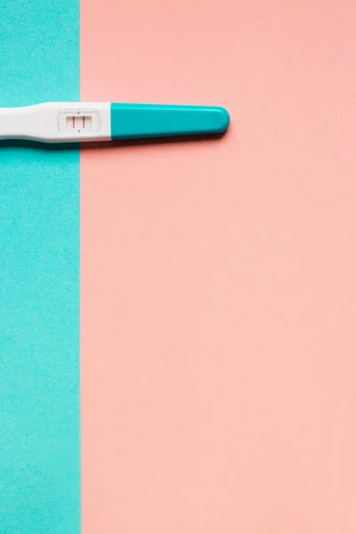 Teste de gravidez de plástico azul positivo em fundo rosa e azul — Fotografia de Stock