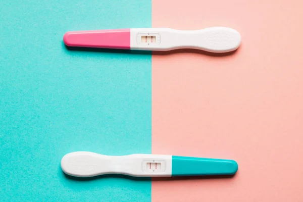 Pozitív rózsaszín és kék műanyag terhességi teszt rózsaszín háttérrel — Stock Fotó