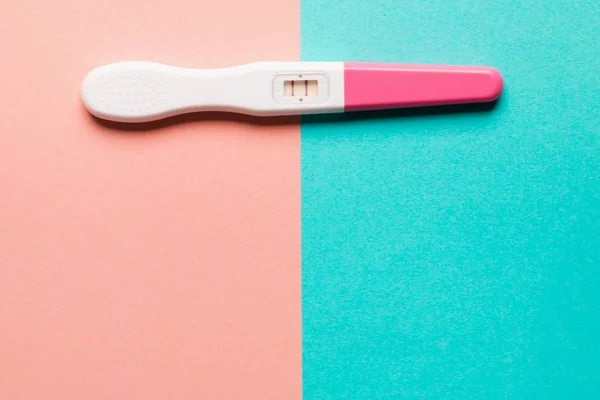 Positive pink plastic pregnancy test on pink and blue background — Stock Photo, Image