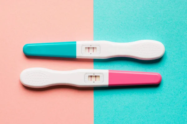 Teste de gravidez de plástico rosa e azul positivo em fundo rosa — Fotografia de Stock