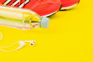 Beyaz kulaklıklar, bir şişe tatlı su ve pembe spor ayakkabılar