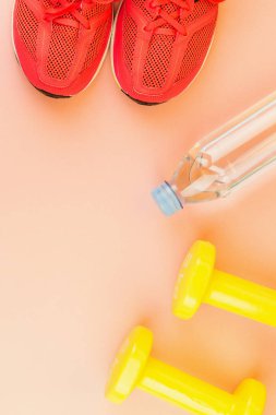 Sarı halter, bir şişe tatlı su ve pembe spor ayakkabılar.