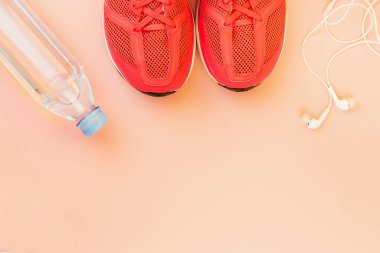 Beyaz kulaklıklar, bir şişe tatlı su ve pembe spor ayakkabılar