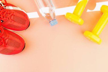 Sarı halter, bir şişe tatlı su ve pembe spor ayakkabılar.