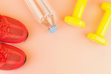 Sarı halter, bir şişe tatlı su ve pembe spor ayakkabılar.