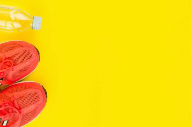 Sarı arka planda bir şişe tatlı su ve pembe spor ayakkabı.