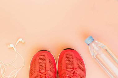 Beyaz kulaklıklar, bir şişe tatlı su ve pembe spor ayakkabılar
