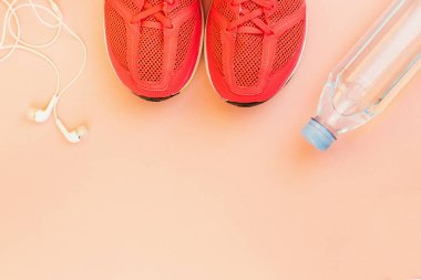 Beyaz kulaklıklar, bir şişe tatlı su ve pembe spor ayakkabılar