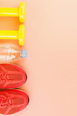 Sarı halter, bir şişe tatlı su ve pembe spor ayakkabılar.