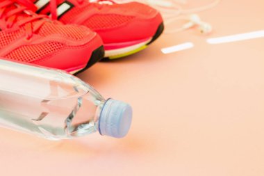 Beyaz kulaklıklar, bir şişe tatlı su ve pembe spor ayakkabılar
