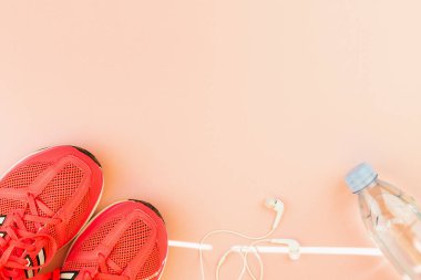 Beyaz kulaklıklar, bir şişe tatlı su ve pembe spor ayakkabılar