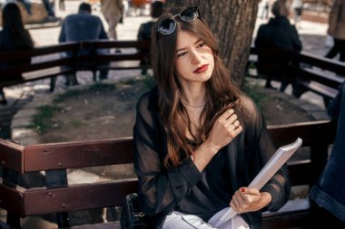 Dergi tutan şehir sokak, bankta oturmuş güzel şık kadın. mutlu hippi kız rahatlatıcı Avrupa şehirde giyinmiş şık kıyafetle