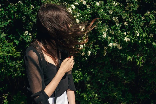 Молодая Женщина Красивыми Ветреными Волосами Позирует Зеленых Кустах Солнечный День — стоковое фото