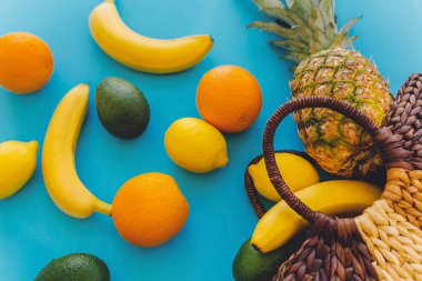 ananas ve muz, portakal, limon, avokado mavi moda Kağıt arka plan üzerinde şık hasır çanta içinde. yaz çok meyve kavramı düz yatıyordu, sağlıklı alışveriş ve tatil vibes