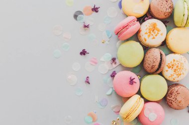 Eflatun çiçekler ve konfeti ile trendy pastel gri kağıt üzerinde lezzetli renkli macaroons, düz yatıyordu. pembe, sarı, yeşil ve kahverengi lezzetli Bademli kurabiye. metin için yer. 
