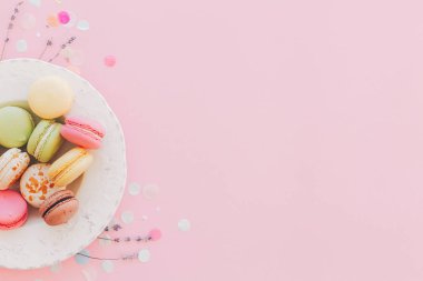 lezzetli renkli macaroons trendy pastel pembe kağıt üzerinde vintage beyaz plaka, modern sanat düz yatıyordu. lezzetli pembe, sarı, yeşil, kahverengi macarons lavanta ve konfeti ile. metin için yer