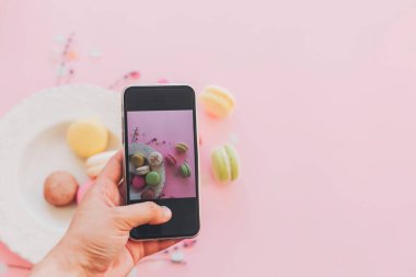 instagram bloglama kavramı, düz yatıyordu. Gıda Fotoğrafçılık. telefon ve şık renkli macaroons alarak fotoğraf vintage plaka trendy pembe kağıt üzerinde tutan el. metin için yer