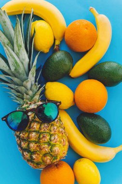 güneş gözlüğü ve muz, portakal, limon, avokado mavi moda Kağıt arka plan, düz üzerinde şık ananas yatıyordu. yaz çok meyve kavramı, sağlıklı yaşam ve parti vibes
