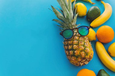 yaz çok meyve kavramı, sağlıklı yaşam ve parti vibes. güneş gözlüğü ve muz, portakal, limon, avokado mavi moda Kağıt arka plan, metin için yer üzerinde şık ananas