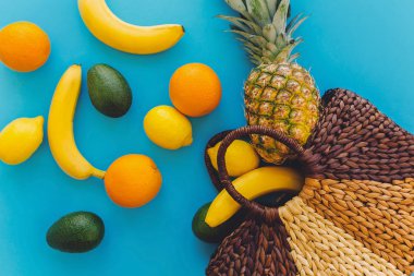 ananas ve muz, portakal, limon, şık hasır çantasından mavi moda Kağıt arka plan üzerine düşen avokado. yaz çok meyve kavramı düz yatıyordu, sağlıklı yaşam tarzı ve parti vibes
