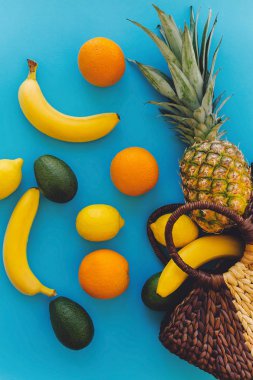 ananas ve muz, portakal, limon, şık hasır çantasından mavi moda Kağıt arka plan üzerine düşen avokado. yaz çok meyve kavramı düz yatıyordu, sağlıklı yaşam tarzı ve parti vibes
