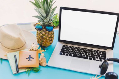 yaz tatil kavramı planlama. boş ekran, güneş gözlüğü ve pasaport, harita, şapka, kabuklar, trendy mavi kağıt masa üstünde defter ananas ile şık dizüstü bilgisayar. seyahat ve yolculuk tutkusu