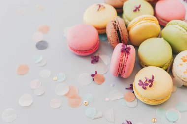 lezzetli pembe, sarı, yeşil ve kahverengi macaroons Lila çiçek ve konfeti ile trendy pastel gri kağıt üzerinde. metin için yer. nefis arka plan