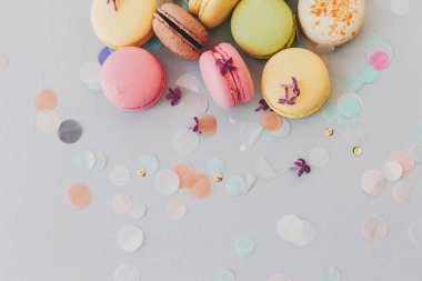 Eflatun çiçekler ve konfeti ile trendy pastel gri kağıt üzerinde lezzetli renkli macaroons, düz yatıyordu. pembe, sarı, yeşil ve kahverengi lezzetli Bademli kurabiye. metin için yer.