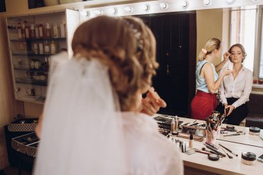 onun makyaj profesyonel sanatçı tarafından sabah hazırlık alma konusunda gelin. büyük ayna ve el kirpik üzerinde koyarak cımbız ile makyaj ustanın önünde güzel gelin